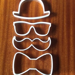 Pode incluir: Cortadores de biscoitos de plástico branco em forma de chapéu, óculos de sol, bigode e gravata borboleta.