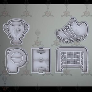 Può includere: Cinque tagliabiscotti in plastica bianca a forma di campo da calcio, porta da calcio, pallone da calcio, scarpa da calcio e trofeo con il numero "#1" sopra.