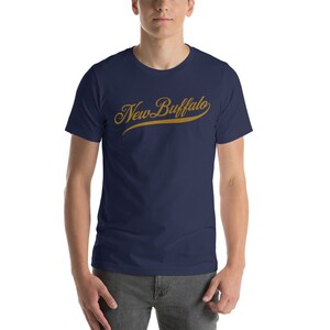 Op de afbeelding: Een marineblauw t-shirt met een gouden scriptontwerp met de tekst "New Buffalo".