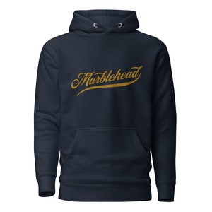 May include: A navy blue hoodie with a gold embroidered logo that says "Marblehead".