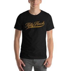 May include: A black t-shirt with a gold "Kitty Hawk" graphic in a cursive font.