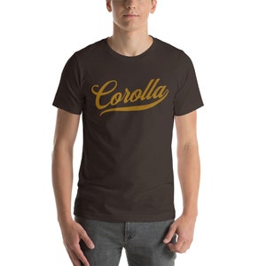 May include: A brown t-shirt with a gold "Corolla" graphic in a vintage baseball font.