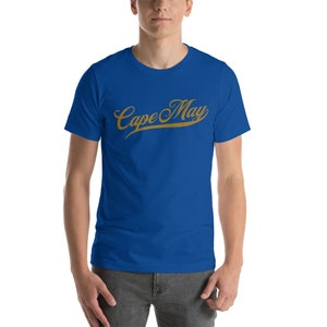 May include: A royal blue t-shirt with a gold script design that reads "Cape May".