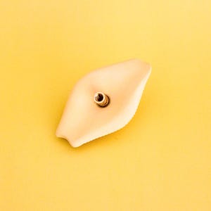 May include: A light beige ceramic incense holder shaped like a boat with a small hole in the centre for incense sticks.