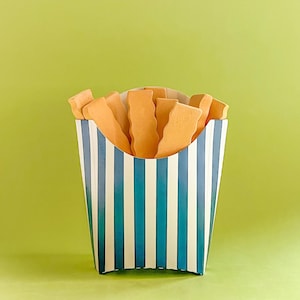 May include: A striped paper container, with blue and white vertical stripes, filled with orange-coloured, wavy-edged biscuits, resembling chips. The container is set against a light green background.