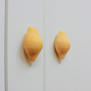May include: Two yellow ceramic cabinet knobs with a ribbed texture in the shape of a teardrop.