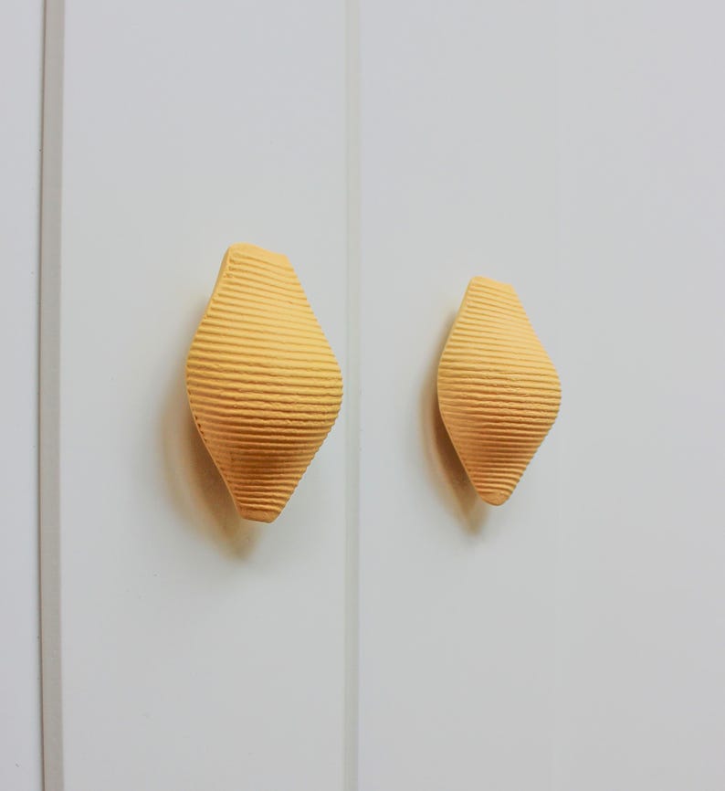 May include: Two yellow ceramic cabinet knobs with a ribbed texture in the shape of a teardrop.