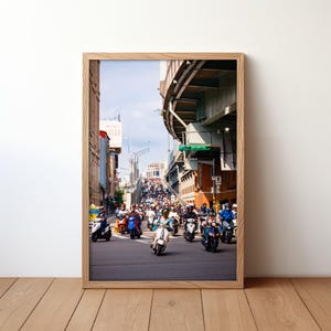 May include: A busy street scene in a city with a large overpass.  Many people are riding scooters and motorcycles up a hill.  The sky is blue and the buildings are mostly brick.