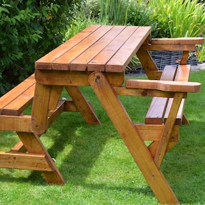 Könnte beinhalten: Ein Picknicktisch aus Holz mit angebrachten Bänken. Tisch und Bänke sind aus hellbraunem Holz gefertigt und stehen auf einer Rasenfläche. Der Tisch ist etwa 152 cm lang.