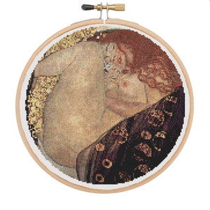 Könnte beinhalten: Eine Kreuzstich-Stickerei, die eine Frau in einem schwarzen und goldenen Kleid zeigt, mit ihrem Haar, das ihr den Rücken herunterfällt. Die Frau ist in einer liegenden Pose dargestellt, mit ihren Armen um sich selbst geschlungen.