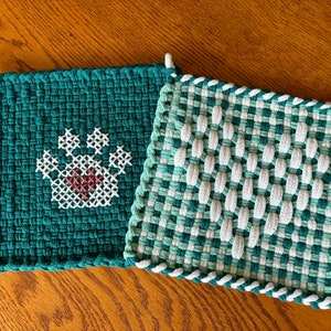 May include: Two green and white woven pot holders. One has a paw print design in red and white.