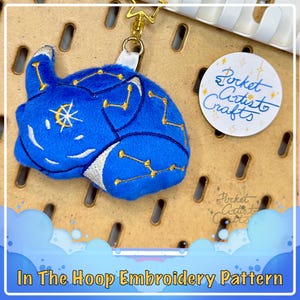 May include: Blue plush toy with gold embroidery of stars and constellations. The toy is attached to a gold key chain with a star charm. The toy is on a brown background with the text "Pocket Artist to Crafts" in a white circle.