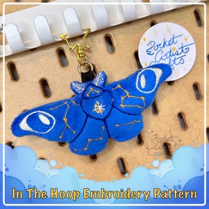Könnte beinhalten: Ein blauer Plüsch-Motte mit goldener Stickerei von Sternen und einem Halbmond. Die Motte ist an einem goldenen Schlüsselanhänger befestigt. Das Bild enthält den Text "Pocket Artist Crafts".