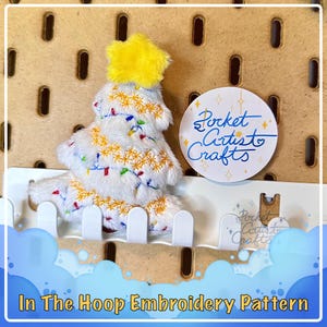May include: White plush Christmas tree with a yellow star on top. The tree is decorated with colorful lights and snowflakes. The tree is sitting on a white picket fence. The image includes the text "Pocket Artist to Crafts".