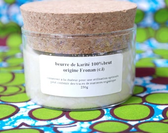 May include: A glass jar with a cork lid filled with a white, solid substance. The label reads "beurre de karité 100% brut origine Fronan (c.i)" and "conserver a la chaleur pour une utilisation optimale peut contenir des traces de matieres organique 230g".