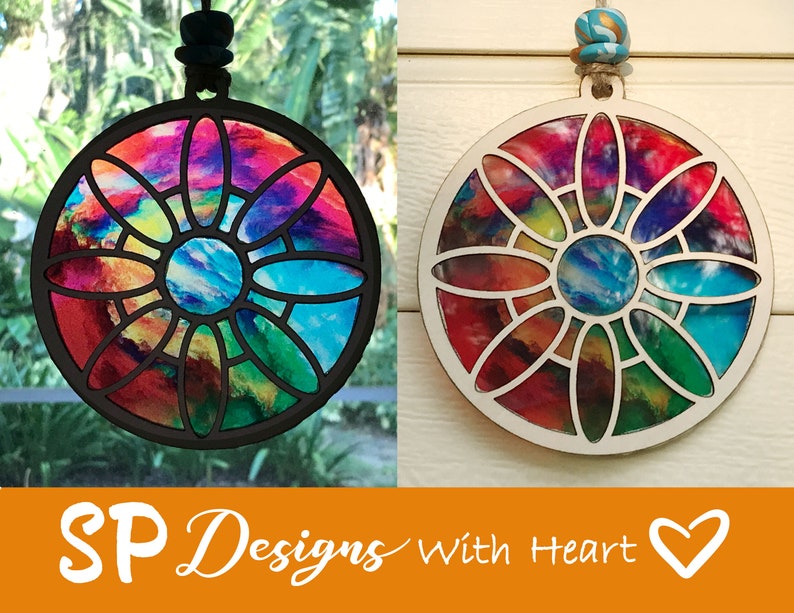 K&ouml;nnte beinhalten: Ein runder, bunter Holzschmuck mit einem Buntglasdesign. Der Anh&auml;nger zeigt eine Blume mit einem blauen Zentrum und ist von einem schwarzen Rahmen umgeben. Der Anh&auml;nger h&auml;ngt an einer Schnur.