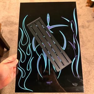 May include: Black artwork with blue and purple flame and abstract designs. A black rectangular stencil is placed diagonally across the artwork. The artwork is signed "VINNY 25".