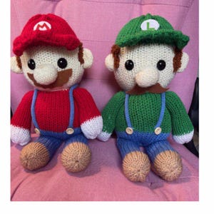 Puede incluir: Figuras de ganchillo de Mario y Luigi, los hermanos italianos, con sus trajes característicos. Mario está en rojo con un sombrero a juego, y Luigi está en verde. El texto "The Italian brothers Mario and Luigi" está en la parte superior.