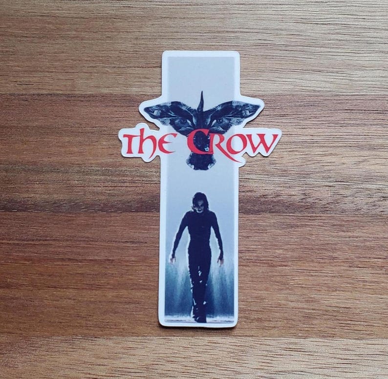 May include: A sticker featuring a black and white image of a crow with the text "The Crow" in red. The crow is flying with its wings spread wide. Below the crow is a black and white image of a person in a dark outfit walking towards the viewer.