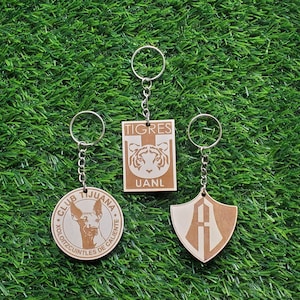 May include: Three wooden keychains with different designs. The first keychain features a brown and white dog with the text "CLUB TIJUANA XOLOITZCUINTLES DE CALIENTE". The second keychain features a tiger with the text "TIGRES UANL". The third keychain features a shield with the letter "A" inside.