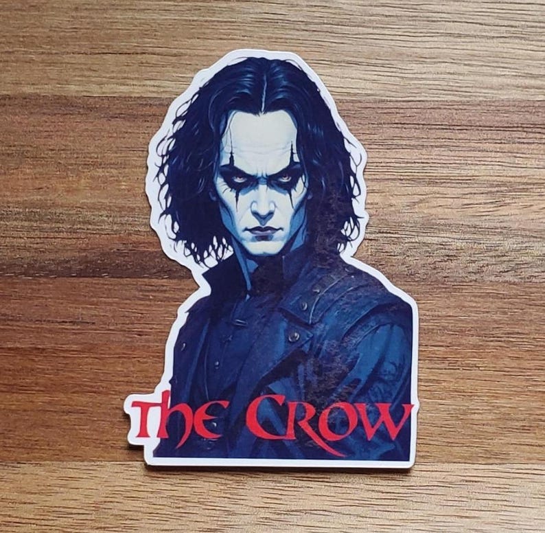 May include: A sticker featuring a close-up portrait of The Crow, a comic book character, with the text "The Crow" in red letters below the image.