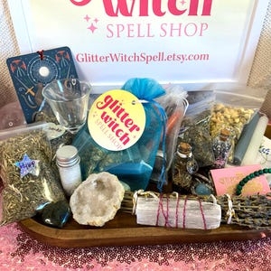 May include: A wooden tray filled with various items, including small glass bottles, bags of herbs, crystals, and a bundle of dried lavender. A sign at the top reads "Witch Spell Shop" and "GlitterWitchSpell.etsy.com".