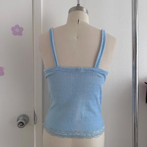 May include: A light blue camisole top with spaghetti straps and a lace trim along the bottom hem. The top is displayed on a mannequin against a white background.