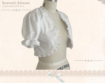 May include: A white bolero jacket with short puff sleeves, ruffled cuffs, and eyelet lace trim along the front opening. The garment is displayed on a mannequin. Text on the image reads: heaven's kittens, handmade with love, Hawaii, never stop dreaming.