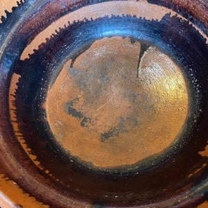 May include: A large, round, terracotta pot with a dark brown glaze. The glaze has a drip effect around the rim of the pot.