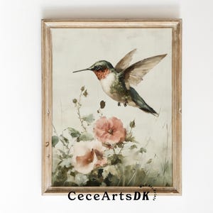 Puede incluir: Una impresión enmarcada de estilo vintage con un colibrí en vuelo sobre flores rosas. El ave tiene plumaje verde, rojo y blanco. La obra de arte está sobre un fondo verde claro y suave, y el marco es de color marrón claro. El texto "CeceArtsDK" es visible.