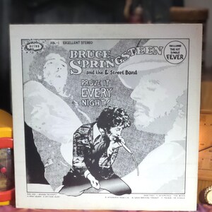 Puede incluir: Una portada de disco de vinilo en blanco y negro con Bruce Springsteen y la E Street Band. La portada muestra el texto Prove It Every Night, incluye el éxito Fever y enumera los títulos de las canciones de la cara uno y dos en la parte inferior.