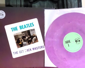 May include: A vinyl record album titled The Beatles The Get Back Masters with a dark brown cover featuring a Trade Mark of Quality pig logo. The record itself is a translucent purple color with a light green center label marked Side 1.