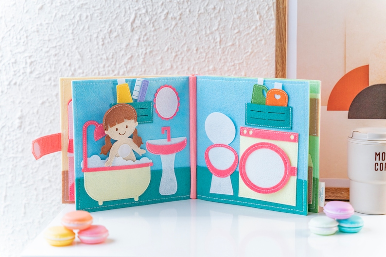 Page 3 and page 4 of dollhouse quiet book, square shaped, made from felt, light and soft, pastel tone colors, with little girl in bathroom sink, wash basins, mirror, laundry room with washing machine and washing liquid