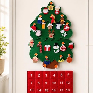 Può includere: Una decorazione da parete in feltro verde a forma di albero di Natale con tronco marrone, arricchita da vari piccoli ornamenti in feltro. Sotto l'albero si trova un calendario dell'Avvento rettangolare rosso con numeri da 1 a 24 in bianco.