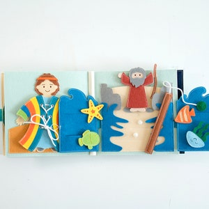 May include: A felt quiet book with a light blue background. The book features felt cutouts of a person, a man with a beard, fish, a starfish, and waves. The book is open, showing multiple pages with different scenes.