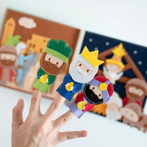 May include: A felt finger puppet set featuring three wise men with crowns, and a felt book with nativity scene illustrations. The puppets are green, blue, and red. The book has a brown and blue background.