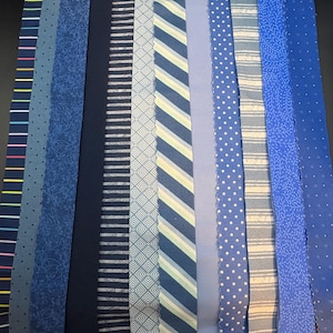 May include: A collection of blue fabric strips with various patterns. Designs include polka dots, stripes, floral, and geometric shapes. The fabrics range in shades from light to dark blue, offering a diverse selection of textures and styles.