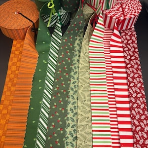 May include: A collection of fabric ribbon rolls featuring various patterns including orange plaid, solid green, green and white diagonal stripes, green with red holly berries, green pine needles, and red and white horizontal stripes and floral prints.