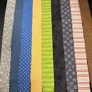 May include: Eight vertical fabric strips with pinked edges. Patterns include a list of US states, blue with white dots, yellow diagonal stripes, lime green horizontal stripes, solid charcoal, gray checkered, red and white stripes, and brown.