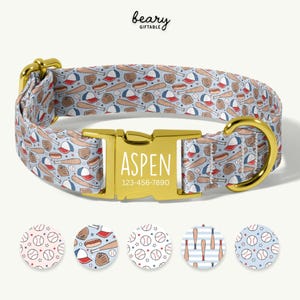May include: A light blue dog collar with a baseball-themed pattern featuring bats, balls, gloves, and hats. The gold-colored buckle is engraved with the name "Aspen" and a phone number. The collar has a gold-colored D-ring.