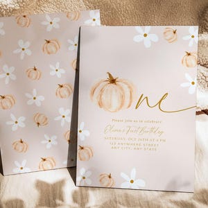 Pu&ograve; includere: Due inviti con sfondo rosa chiaro. Uno presenta una zucca ad acquerello e la parola "one" in oro. L'altro ha un motivo di zucche e fiori bianchi. Il testo sull'invito recita "Olivia's First Birthday".