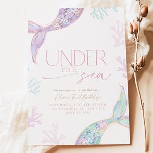 May include: A rectangular invitation card with the text "UNDER THE SEA" and mermaid tail illustrations. The card includes event details: "Olivia's First Birthday" on Saturday, August 4th at 4 PM. Coral and seaweed designs decorate the card.