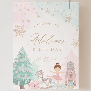 以下が含まれることがあります： 金色の雪片が散りばめられたピンクとブルーの水彩画の背景。 「Adeline's Birthday 02.25.24へようこそ」という文字が金色の筆記体で書かれています。 緑色のクリスマスツリーの前で、バレリーナ人形がナッツクラッカー人形の隣に立っています。 下部に「our dearest moments design co.」という文字が金色の筆記体で書かれています。