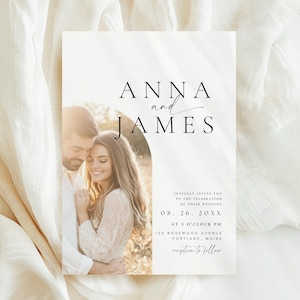 May include: A wedding invitation featuring a photograph of a couple, with the names "ANNA and JAMES" in elegant script. The invitation includes event details: date, time, and location. The design is minimalist with a soft, romantic aesthetic, set against a neutral background.