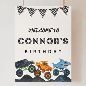 May include: A white poster with the text "Welcome to Connor's Birthday" and three monster truck illustrations. The trucks are purple, orange, and blue, with black and white checkered flags at the top.