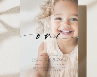 May include: A rectangular birthday invitation card featuring a large photograph of a smiling child. The card displays the number one in a large, semi-transparent font, the word one in black script, and text detailing Olivia's First Birthday.