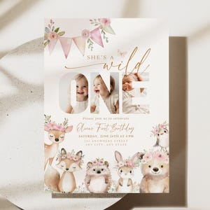 Könnte beinhalten: Eine Geburtstagseinladung mit dem Text "She's a Wild One" und "One" mit drei Fotos eines Babys. Die Einladung zeigt Aquarellillustrationen von Waldtieren und floralen Akzenten. Die Einladung enthält Datum, Uhrzeit und Ort.