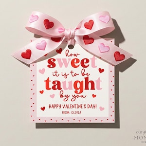 May include: A Valentine's Day gift tag with a pink ribbon decorated with heart shapes. The tag says "how sweet it is to be taught by you" and "Happy Valentine's Day!" in red and pink. The tag is from Olivia.
