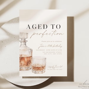 May include: A rectangular birthday invitation card featuring a watercolor illustration of a glass decanter and a tumbler filled with amber liquid. The text reads AGED TO PERFECTION, Please join us to celebrate, John's 50th birthday, SATURDAY, JUNE 26TH AT 4 PM, 123 ANYWHERE STREET, ANY CITY, ANY STATE, and RSVP by June 1st TO SAM 555-123-4567.
