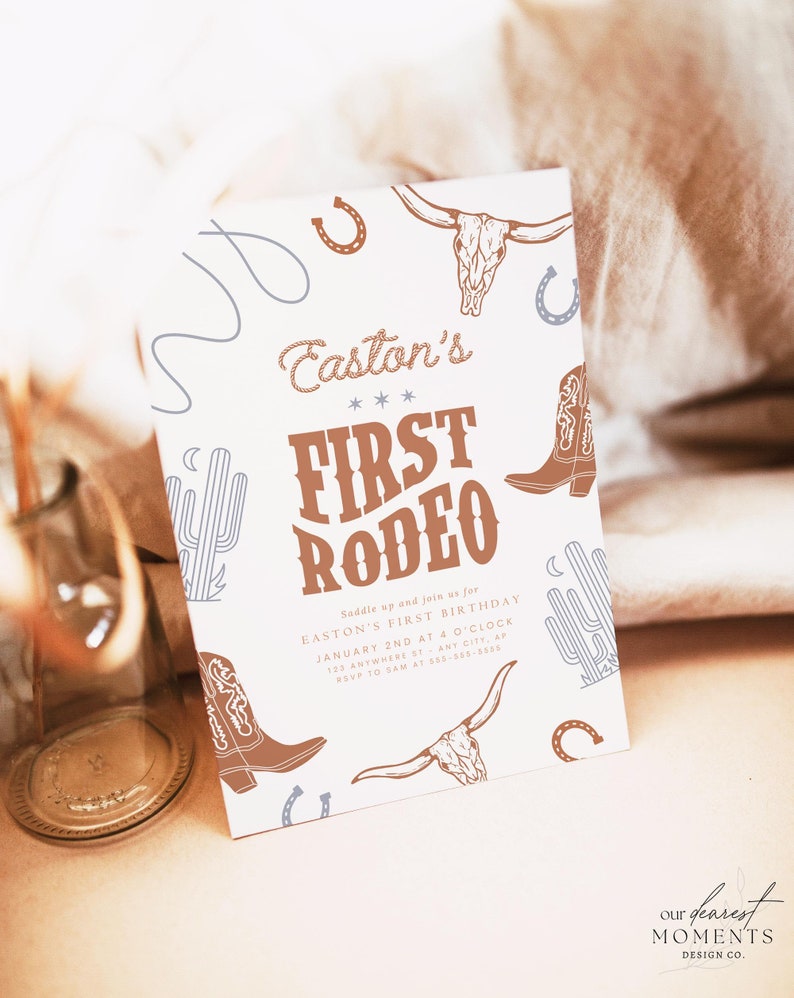 May include: A rectangular invitation card with a rodeo theme. The card features illustrations of cowboy boots, a bull skull, cacti, and horseshoes. The text reads "Easton's First Rodeo" in a brown, vintage font. The card is on a neutral background.